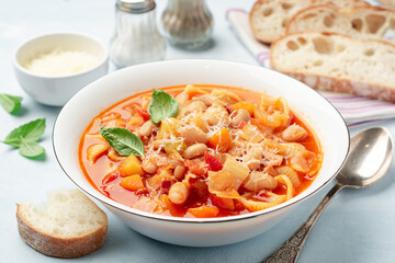 Italian minestrone soup with parmesan cheese and basil on blue concrete background