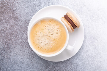 Close-up of cup with coffee and chocolate macaron on white plate. Concept of coffee break, top view