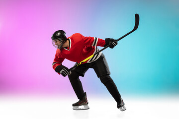 Fototapeta na wymiar On fire. Male hockey player with the stick on ice court and neon gradient background. Sportsman wearing equipment, helmet practicing. Concept of sport, healthy lifestyle, motion, wellness, action.