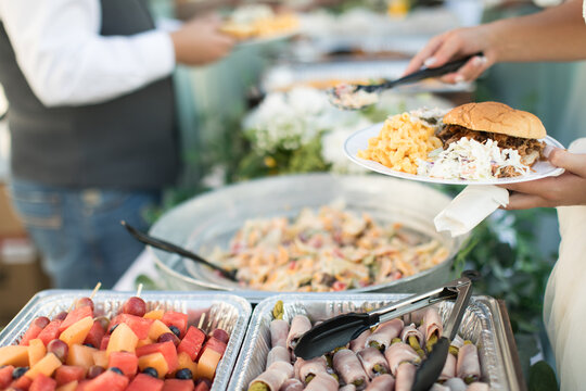 Close up of bridal party dishing up catered buffet food at casual outdoor wedding