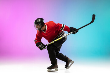 First. Male hockey player with the stick on ice court and neon gradient background. Sportsman wearing equipment, helmet practicing. Concept of sport, healthy lifestyle, motion, wellness, action.