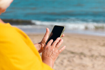Close-up of a cheerful young blonde in a summer hat uses a smartphone near the sea