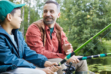 Portrait of happy father enjoying fishing with little son during camping trip by lake