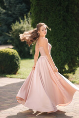 Beautiful young woman spin arround in gorgeous evening dress, background of green thee
