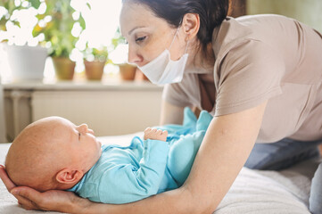 Beautiful mother in protective face mask holding her little cute newborn son protecting him from viruses and infections. Coronavirus covid-19 prevention. Home quarantine. Happy family at home.