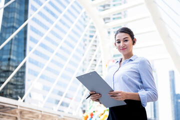 Portrait images of Caucasian business woman or secretary, Standing, looking and holding the report, On  blur building background, to people and business work concept.