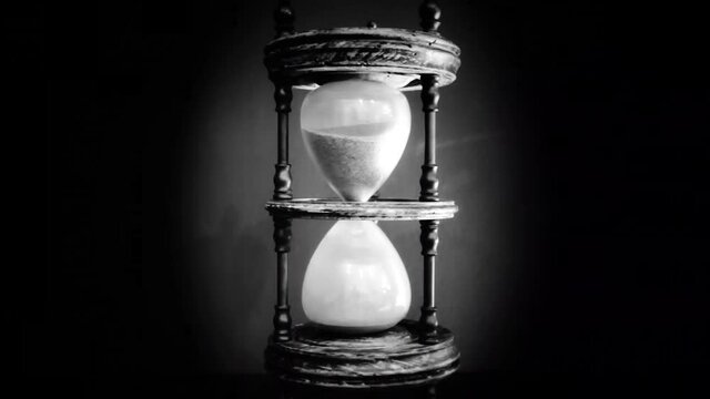 A cool desaturated shot of sand falling from the top of a hourglass (an ancient device for the measurement of time).

