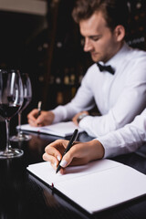 Selective focus of sommeliers writing on notebooks near glasses of wine on table