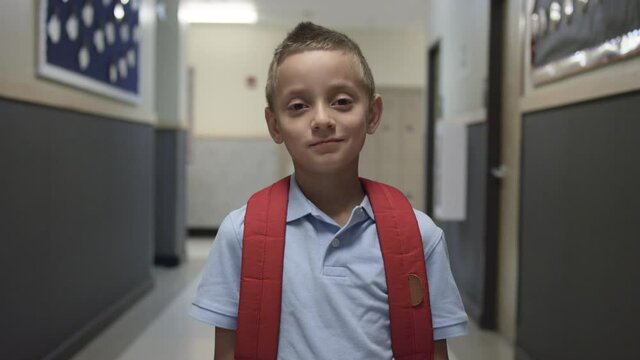 Elementary or Primary school boy with backpack stares at camera in school hall