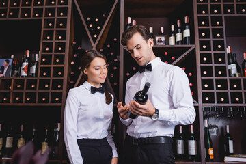 Sommeliers looking at bottle of wine near rack in restaurant
