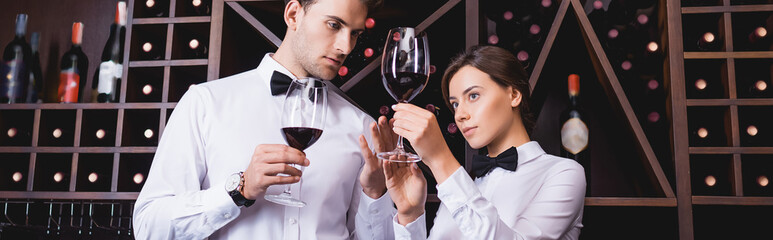 Panoramic shot of sommelier looking at glass of wine near colleague in restaurant