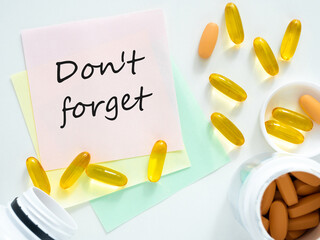 Reminder with text on a piece of paper: don't forget. Colored stickers and a handful of pills are on the table, flatley, copy space, top view. The concept for the reminder about taking vitamins