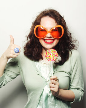 woman in big orange glasses licking lollipop with her tongue