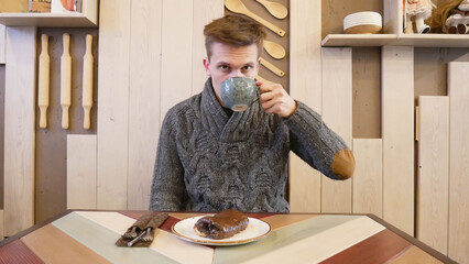 Guy in a sweater drinks a cappuccino and sits in a cafe. Baking chocolate with poppy seeds lies on a saucer in the foreground. Breakfast in the cafe, croissant and drinks are shown.