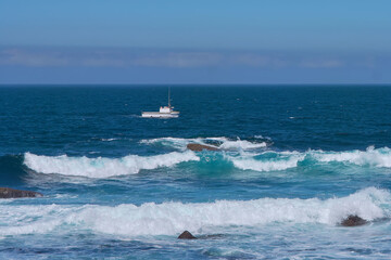 Obraz premium Fishing boat sailing near the Punta de la Barca lighthouse in the fishing village of Muxía, Costa da Morte, Galicia, Spain