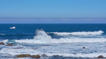 Fishing boat sailing near the Punta de la Barca lighthouse in the fishing village of Muxía, Costa da Morte, Galicia, Spain