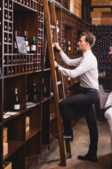 Selective focus of sommelier standing on ladder near racks with wine bottles