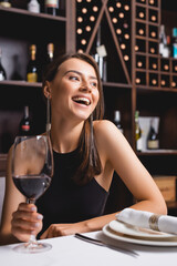 Selective focus of elegant woman laughing while holding glass of wine in restaurant