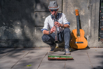 A busker street musician playing music with clarinet on a city sidewalk.