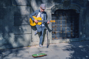 A busker street musician playing music with guitar on a city sidewalk.