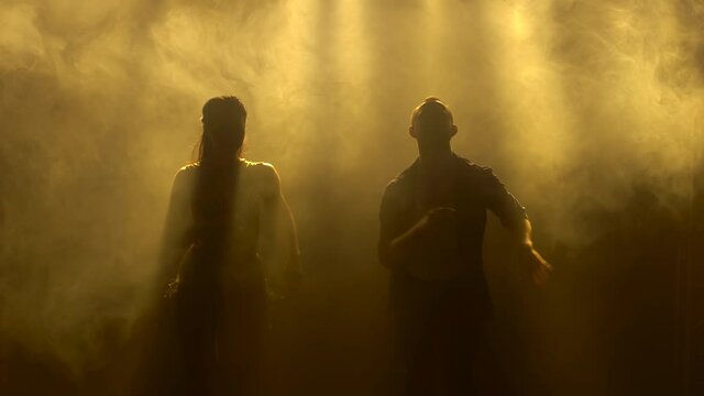 A couple of young dancers dancing a passionate Latin American salsa dance surrounded by yellow lights. Silhouettes of a man and a woman move their hips to the beat of the music. Close up.
