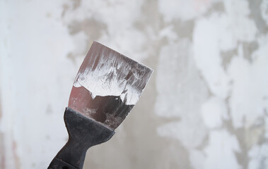Hand with putty knife or metal spatula repairing wall rough surface