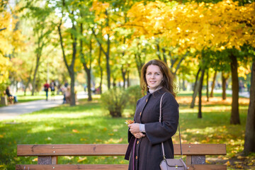 Young woman with autumn leaves in hand and fall yellow maple garden background