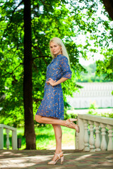 Portrait of a young blonde woman in blue dress walking in summer parkpark