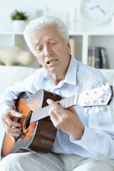Fototapeta premium Happy senior man with guitar sitting on the sofa at home