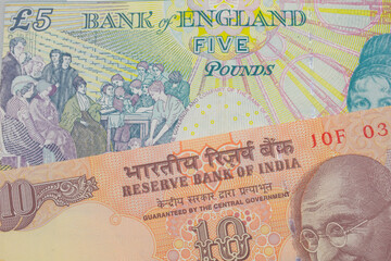 A macro image of a orange ten rupee bill from India paired up with a colorful, five pound bank note from the United Kingdom.  Shot close up in macro.
