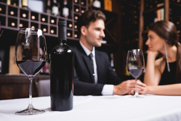 Selective focus of bottle and glass of wine on table near young couple holding hands in restaurant