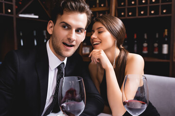 Selective focus of man in suit sitting near glasses of wine and elegant girlfriend in restaurant