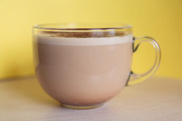 a mug of coffee with milk sprinkled with chocolate chips, and foam, on a yellow background. Energy and cheerfulness in the morning.