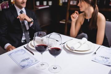 Selective focus of glasses of wine and menu on table near young couple in restaurant