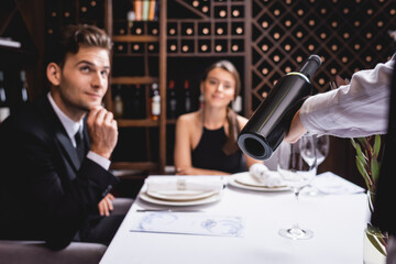Selective focus of sommelier holding bottle of wine near elegant couple in restaurant