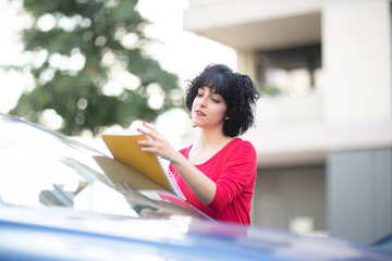 Frau mit rotem Kleid checkt gelbes Ringbuch am blauen Auto