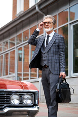 Fototapeta na wymiar senior caucasian entrepreneur next to his rich automobile, handsome male stand in the street, elegant and stylish, in formal suit