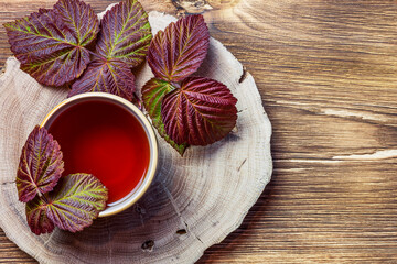 Morning evening relaxing warming medicinal aromatic tea from raspberry leaves in a cup anti-inflammatory antipyretic sedative, flat layout on natural wooden background