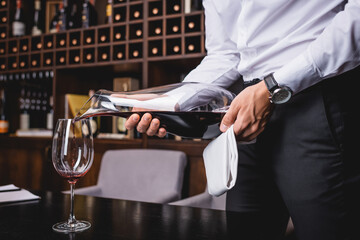 Cropped view of sommelier pouring red wine from decanter in glass - obrazy, fototapety, plakaty