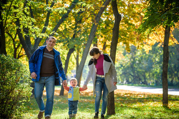 Obraz premium Beautiful young family on a walk in autumn forest on maple yellow trees background. Father and mother hold son on hands. Happy family leisure together concept