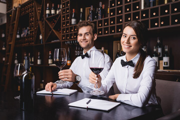 Selective focus of sommeliers with glasses of wine looking at camera in restaurant