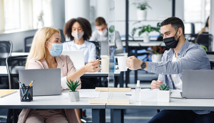 Coffee break in modern office and protecting health of workers. Young man and woman in protective masks clink cups through glass board in interior of office