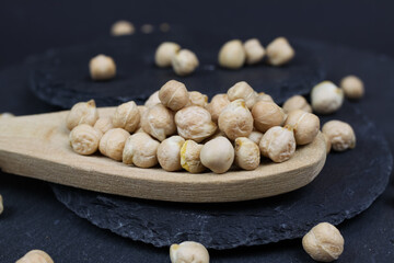 Macro closeup of isolated wood spoon with raw uncooked chickpeas (channa dhal) on black slate stone...