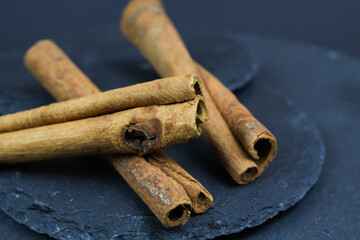 Macro closeup of three isolated dried cinnamon sticks on black slate stone background