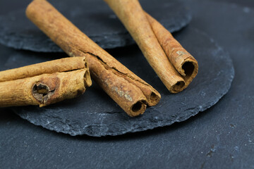 Macro closeup of three isolated dried cinnamon sticks on black slate stone background