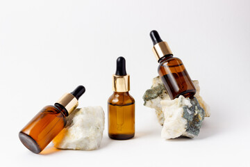 Natural cosmetics in glass bottles with a dropper stand next to a stone on a beige background with bright sunlight. The concept of natural cosmetics, natural essential oil