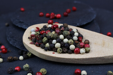 Macro closeup of isolated dried green, black and red mixed peppercorns with isolated wood spoon on slate stone background (focus on center)