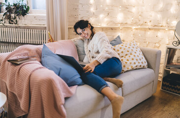 Fototapeta premium Cheerful woman resting on couch with laptop and smartphone