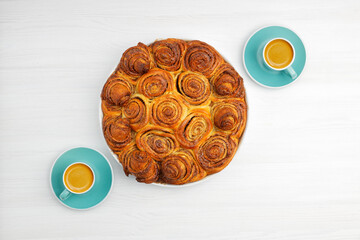 Homemade cinnamon rolls from yeast dough and two cups of coffee espresso on white wooden table. Top view. Copyspace.