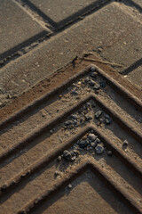 Old rusty metal hatch in the sand on the background of street tiles.